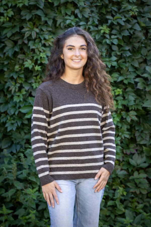 Femme portant le Pull Clun beige Kascha à rayures marron, assise en terrasse, style décontracté chic.
